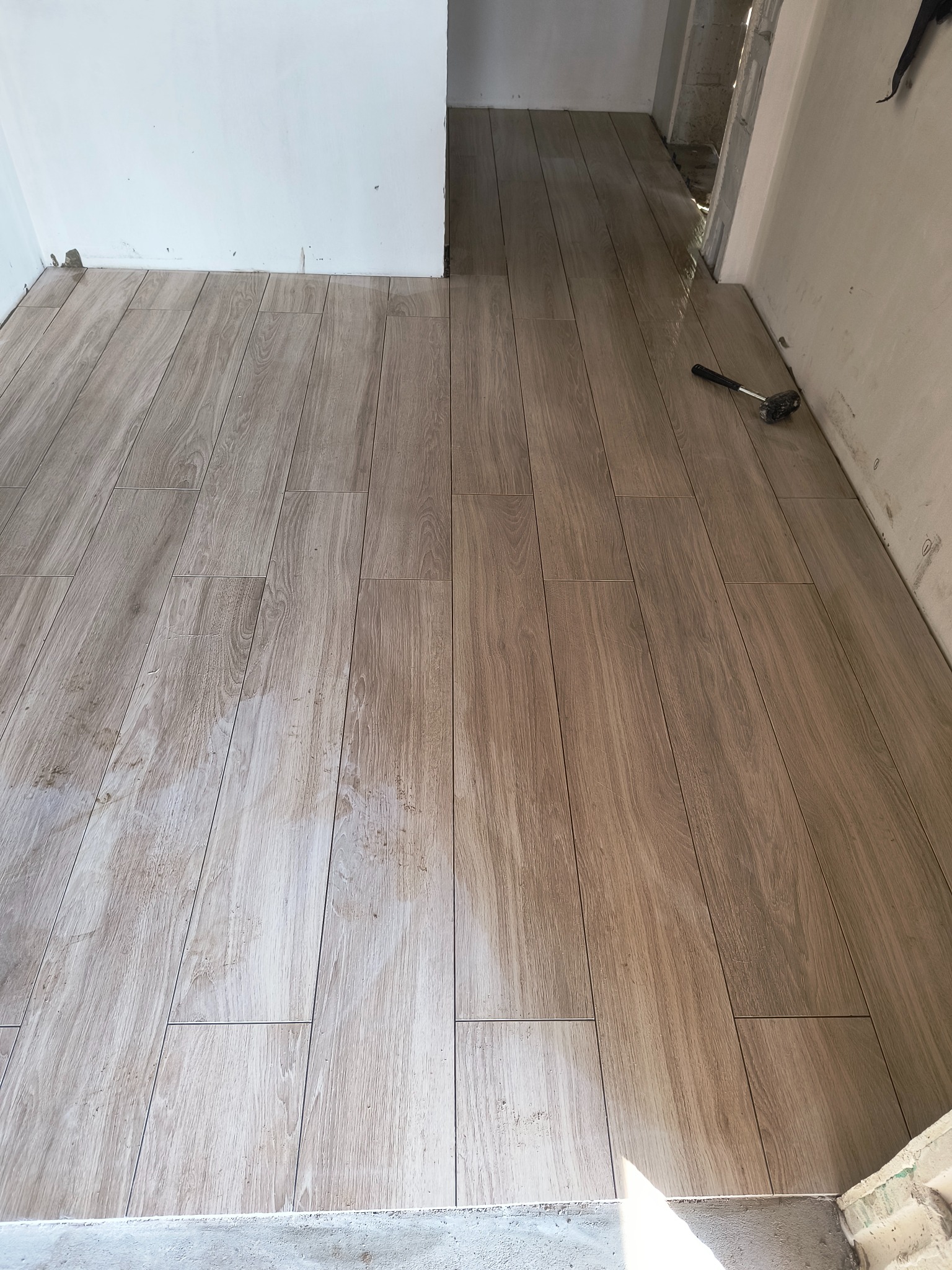 Ułożona podłoga z płytek imitujących drewno w jasnym odcieniu, widoczny gumowy młotek przy ścianie, surowy stan ścian.