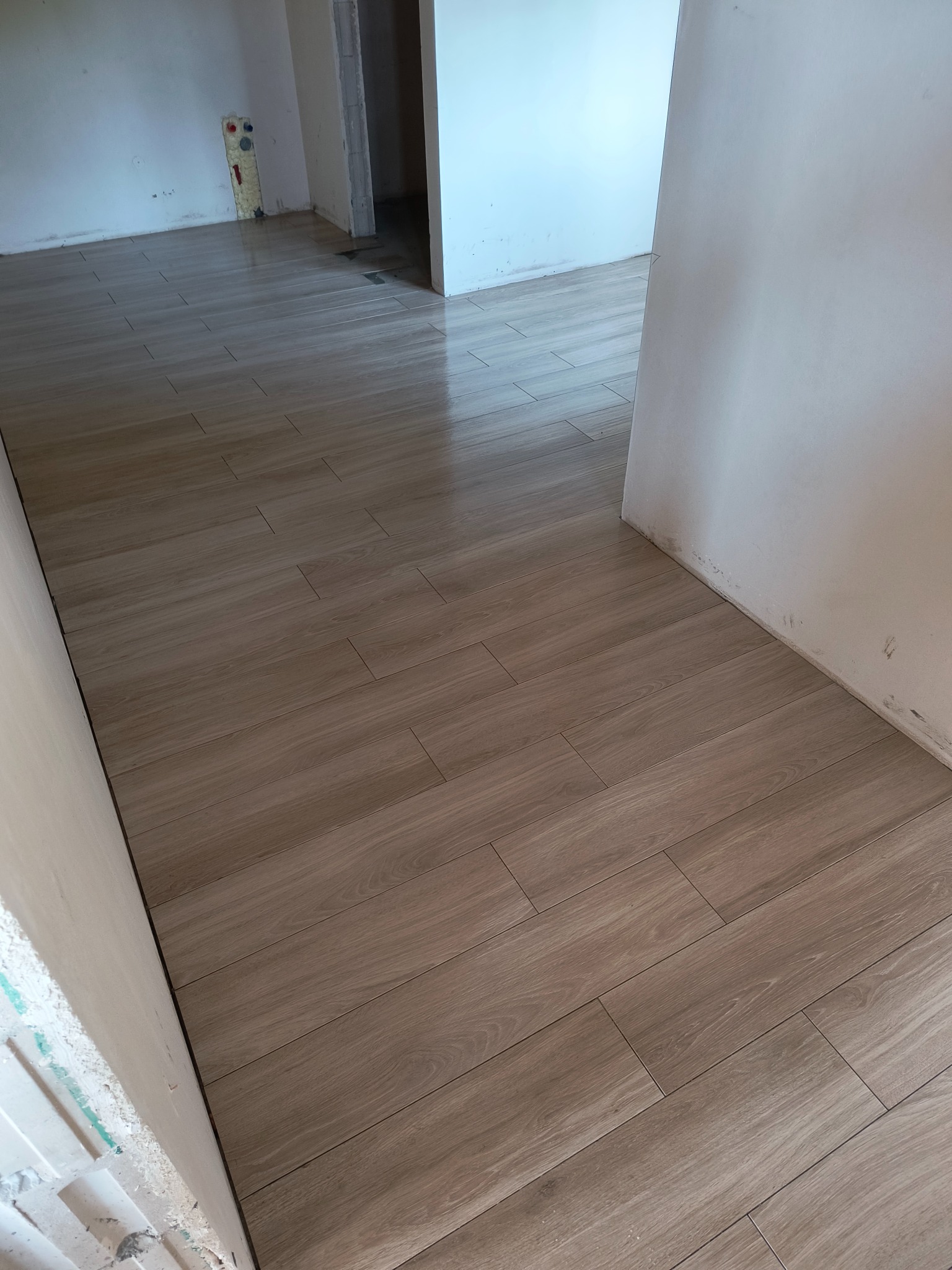 Ułożone płytki podłogowe imitujące drewno w trakcie remontu, widoczne niedoskonałości na ścianach oraz instalacja wodna w tle.