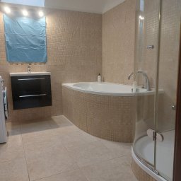 USŁUGI REMONTOWO BUDOWLANE ROBERT PIOTROWSKI - Jasna łazienka z mozaiką, kabiną prysznicową i wanną narożną. Umywalka z szafką w kolorze czarnym. Okno dachowe. Całość utrzymana w ciepłej tonacji beżu i brązu.