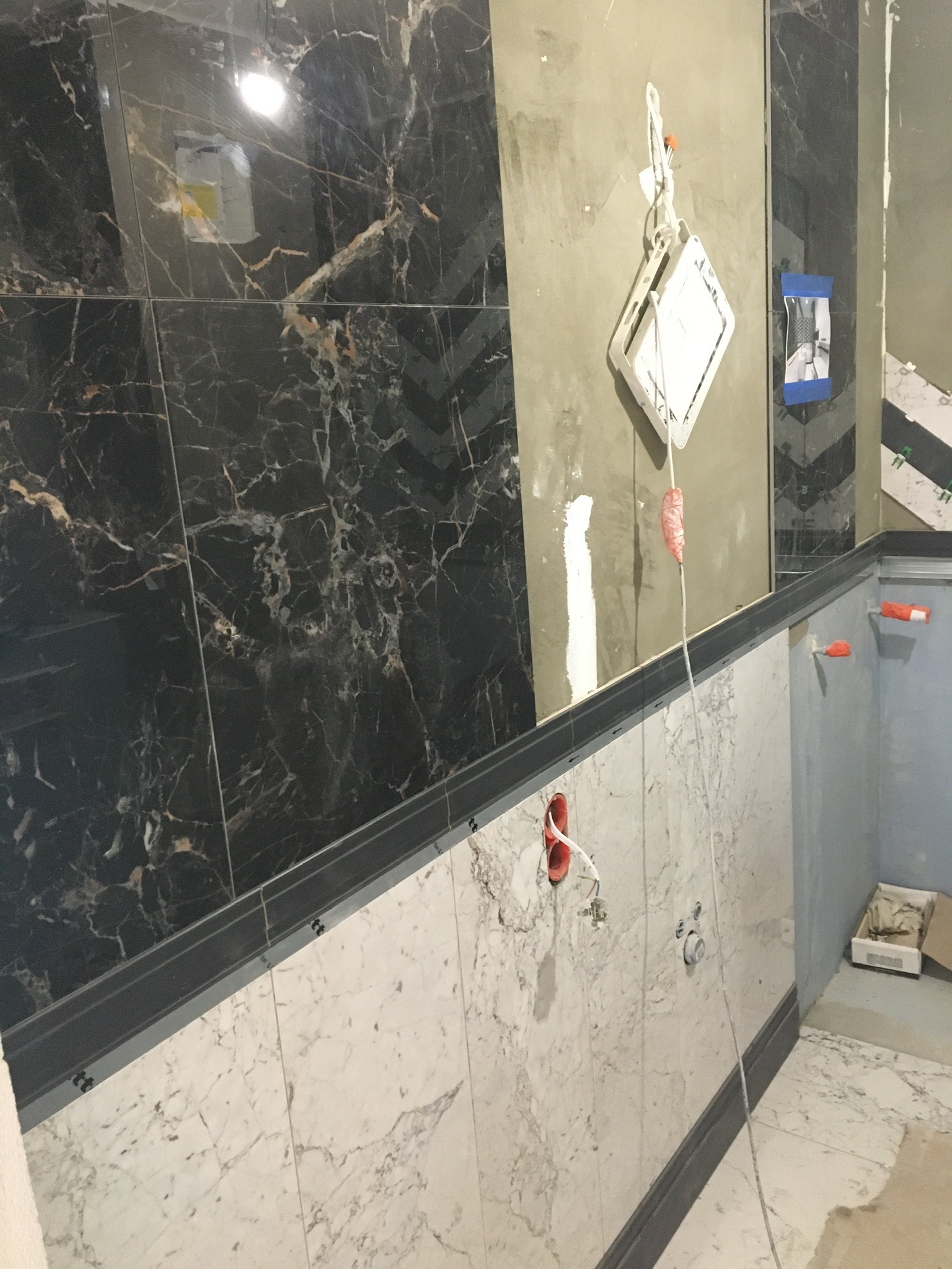 Fragment łazienki w trakcie prac wykończeniowych: położone marmurowe płytki w dwóch kolorach (czarnym i białym), widoczne kable elektryczne, niedokończone ściany i elementy montażowe.