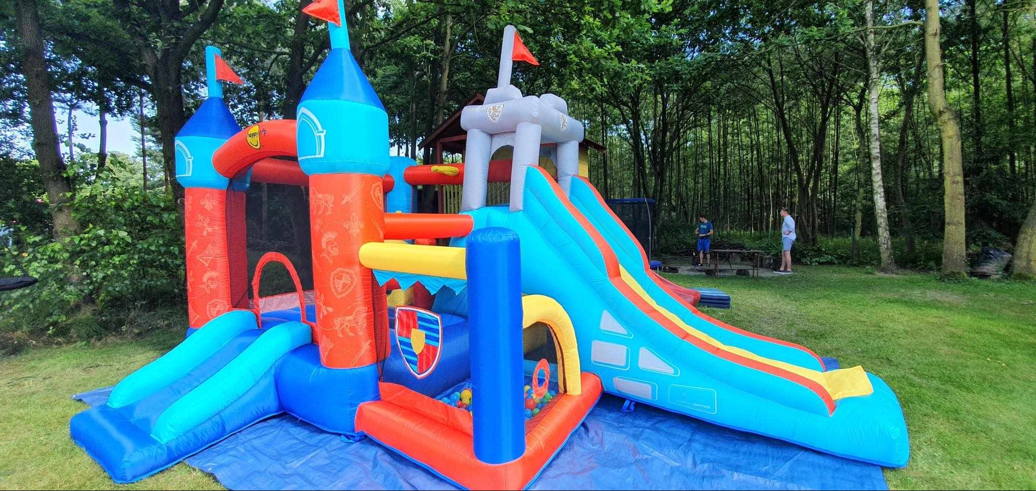 Kolorowy dmuchany zamek ze zjeżdżalnią i wieżami na trawie w Stawkach, widoczne osoby w tle.