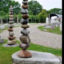 Kamienne wieże w Legnicy, ułożone z różnej wielkości i koloru kamieni, na tle zieleni i żwirowej ścieżki.