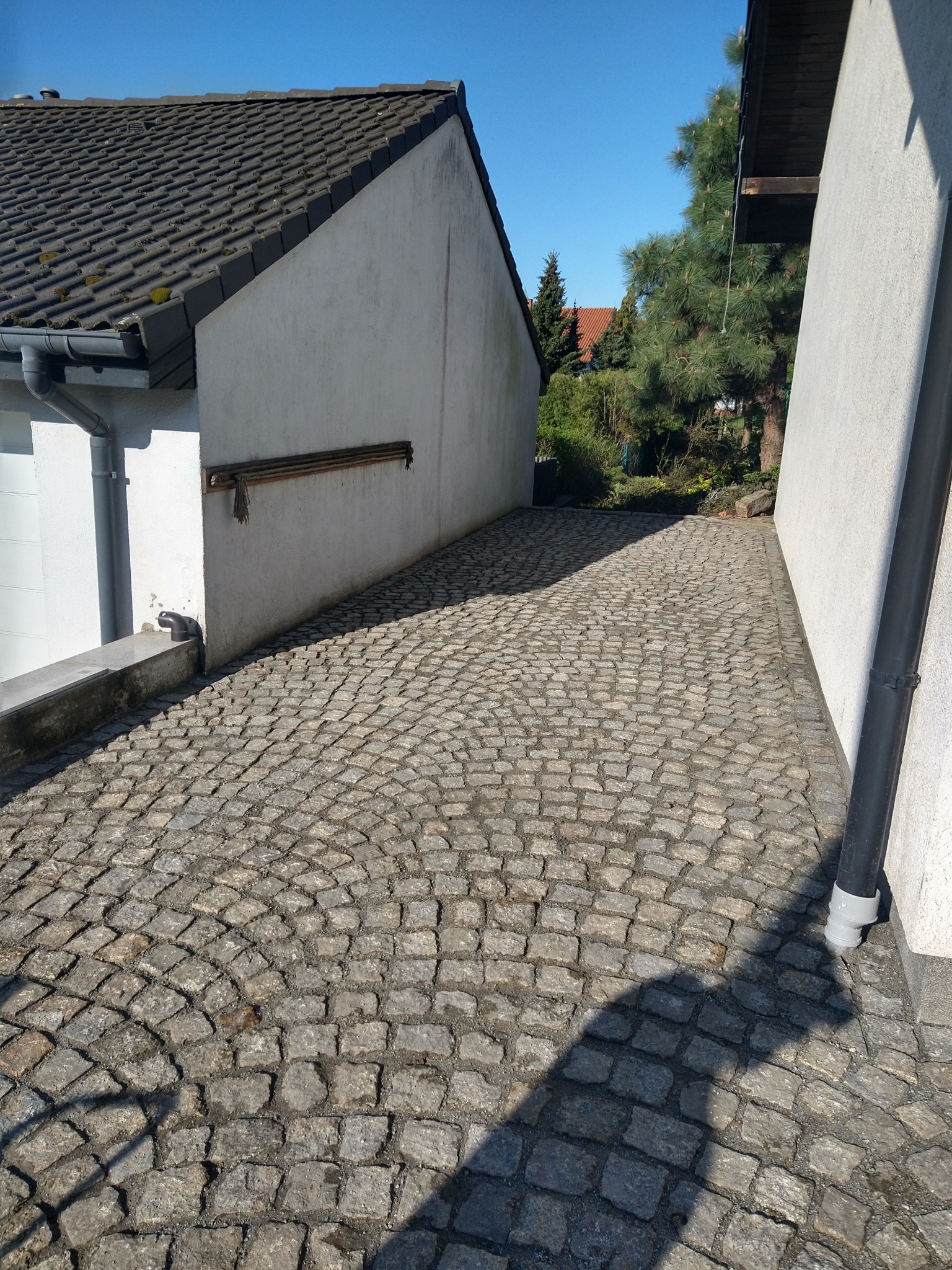 Ułożona nawierzchnia z kostki granitowej w wąskim przejściu między budynkami, widoczne rury spustowe i cień rzucany na kostkę.