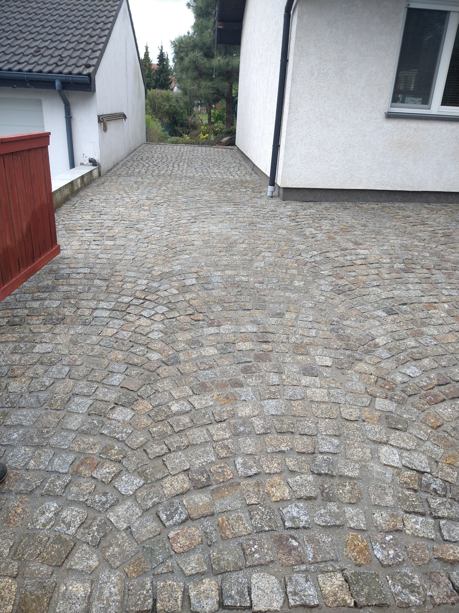 Ułożona kostka granitowa na podjeździe między dwoma budynkami, widoczne nieregularne kształty kamieni i łukowy wzór ułożenia.