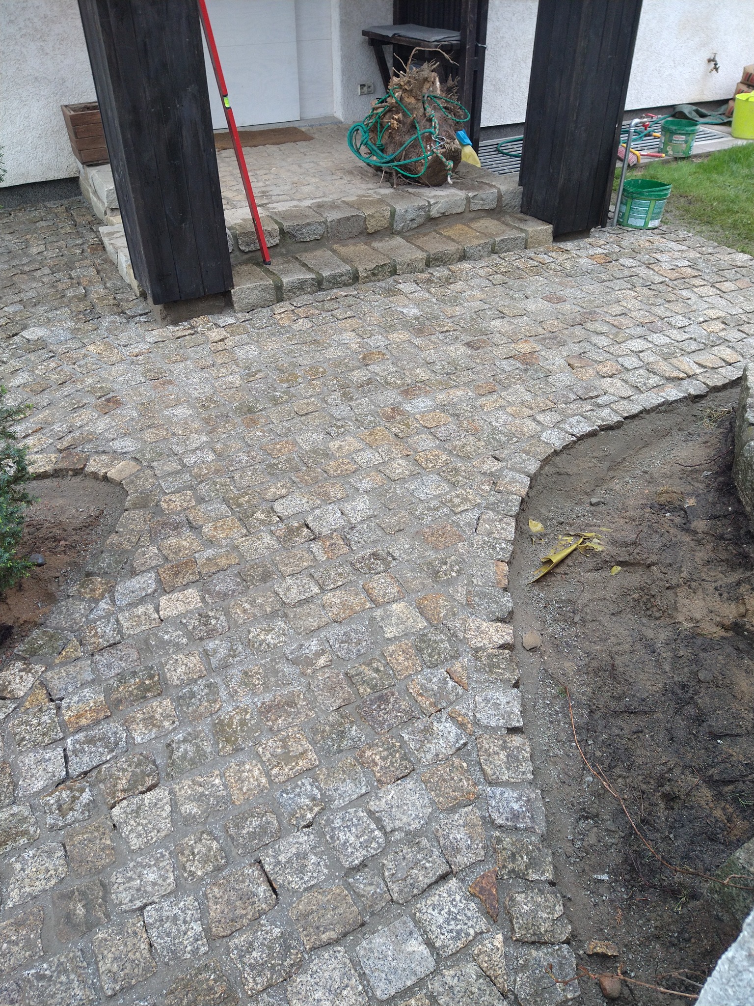 Układanie kostki granitowej w Poznaniu, widok z góry na częściowo ukończony chodnik z nieregularnych szaro-złotych kostek, obok rabata ziemi.