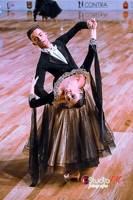 Para tancerzy w strojach galowych prezentuje taniec towarzyski w Parczewie, kobieta w pochyleniu z ozdobnym dekoltem, mężczyzna w smokingu.