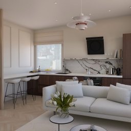 Revelo Wioletta Pietras - Wnętrze mieszkania z aneksem kuchennym, białym narożnikiem i lampą wiszącą. Widok na miasto przez okno. Aranżacja w jasnych, neutralnych barwach.