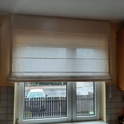 Problind Warszawa - Jasna, kremowa roleta rzymska zamontowana w oknie kuchennym, widok na ulicę i ogrodzenie w tle.