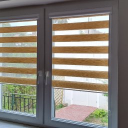 Problind Warszawa - Okna PCV z zamontowanymi beżowo-białymi roletami w systemie dzień i noc, widok na ogród z kostką brukową i białymi drzwiami.