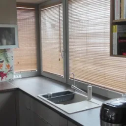 Kuchnia z trzema oknami przesłoniętymi drewnianymi żaluzjami poziomymi, widok na zewnątrz, nowoczesny wystrój.