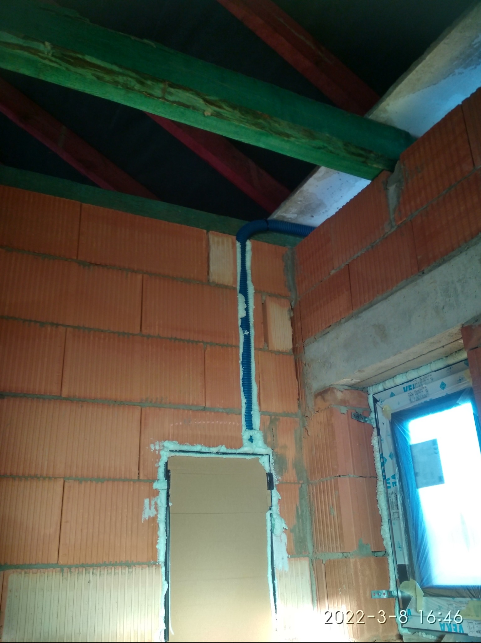 Wewnętrzna ściana z pustaków ceramicznych z pionowo ułożonym, niebieskim peszlem instalacyjnym, zabezpieczonym pianką montażową. Widoczne drewniane elementy konstrukcji dachu.