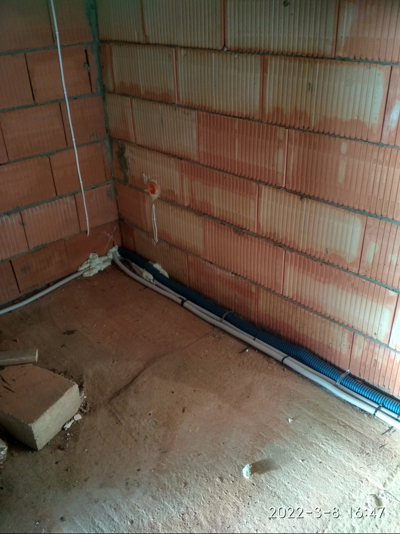 Wnętrze budynku w trakcie prac instalacyjnych: kable w peszlach ułożone wzdłuż ściany z czerwonej cegły dziurawki, zabezpieczone pianką montażową.