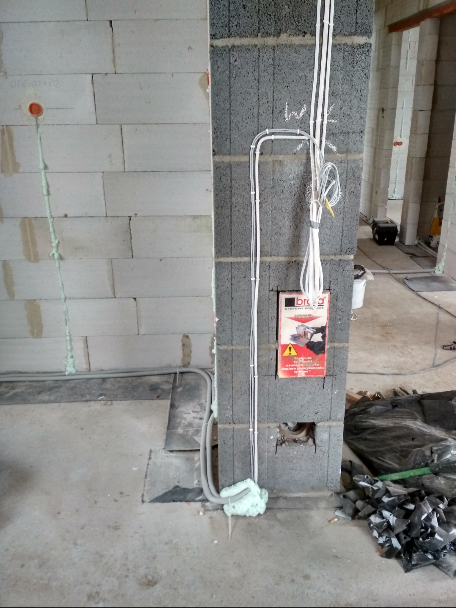 Instalacja elektryczna w surowym budynku w Kobylej Górze. Widoczne kable w peszlach przymocowane do ściany z bloczków, puszka instalacyjna i pianka montażowa.