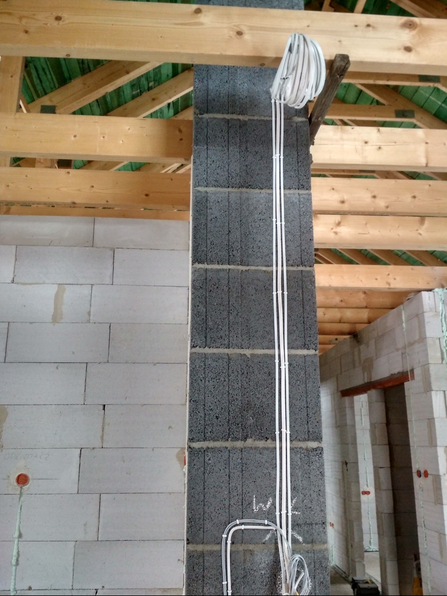 Wewnętrzna instalacja elektryczna w surowym budynku z szarych bloczków, kable przymocowane do ściany, widoczne drewniane elementy konstrukcji dachu.