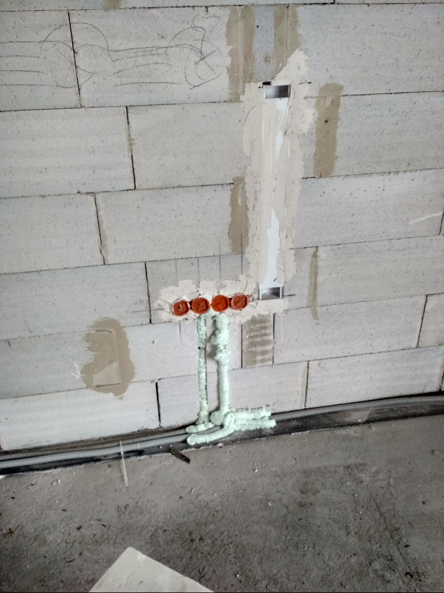 Wewnętrzna instalacja elektryczna w ścianie z betonu komórkowego, z widocznymi puszkami pod gniazdka i peszlami zabezpieczonymi pianką montażową. Etap prac wykończeniowych.