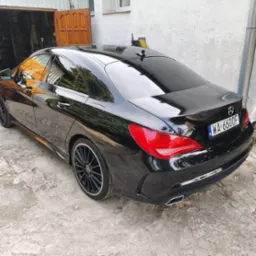 Błyszczący, czarny Mercedes-Benz CLA po umyciu, zaparkowany na betonowym podjeździe przed garażem z otwartymi drewnianymi drzwiami.