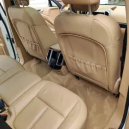 Beżowe skórzane tylne siedzenia i dywaniki w samochodzie po czyszczeniu, widoczne ślady odkurzania.