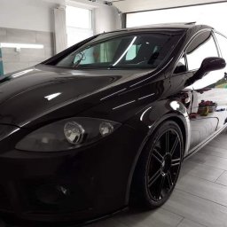 Autohaus Mar car Tomasz Zauer - Błyszczący, czarny samochód Seat Leon po detailingu, z widocznymi odbiciami w lakierze, stojący w garażu z butlami gazowymi w tle.