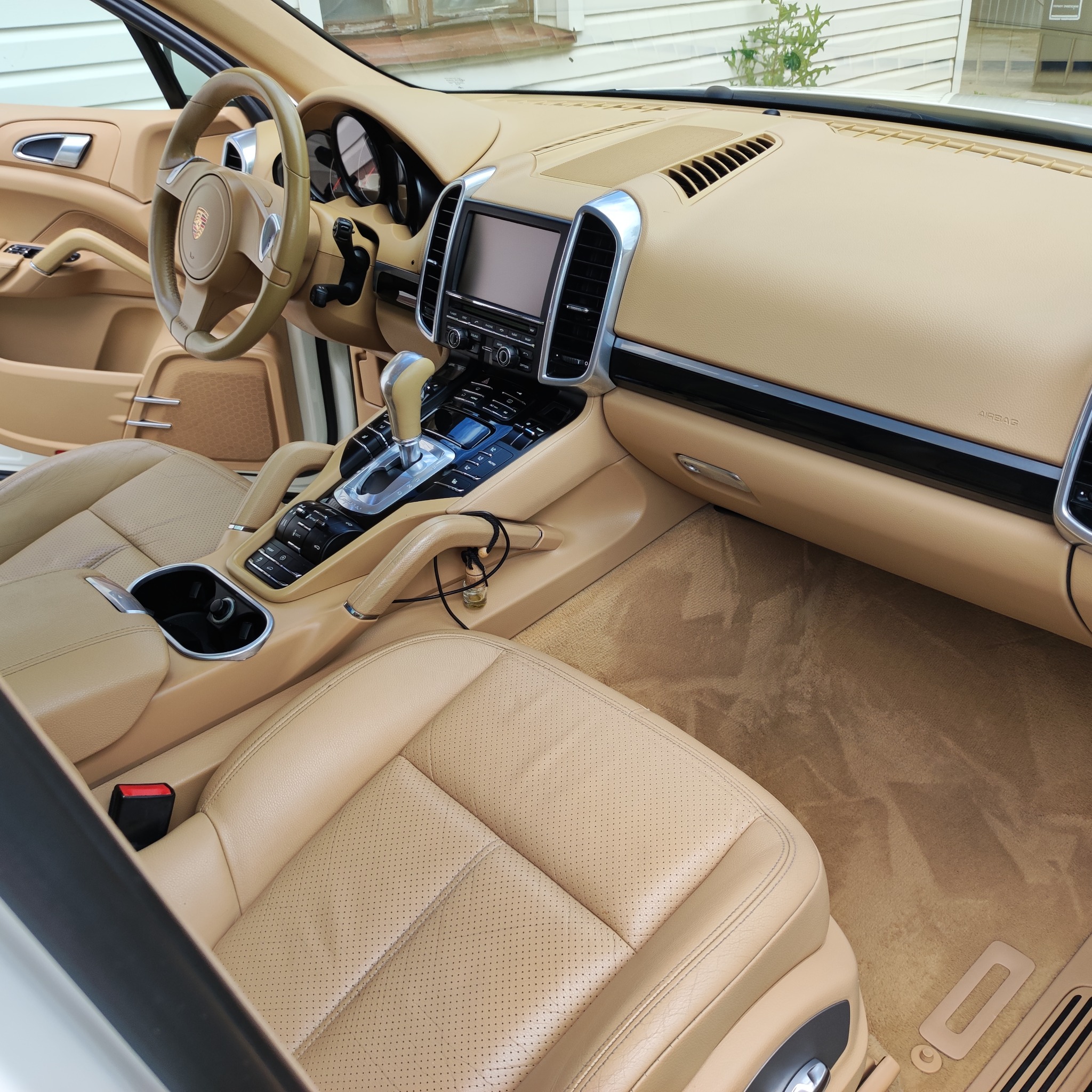 Jasnobeżowe wnętrze samochodu Porsche Cayenne, widok na deskę rozdzielczą, fotele skórzane z perforacją i dywaniki podłogowe.