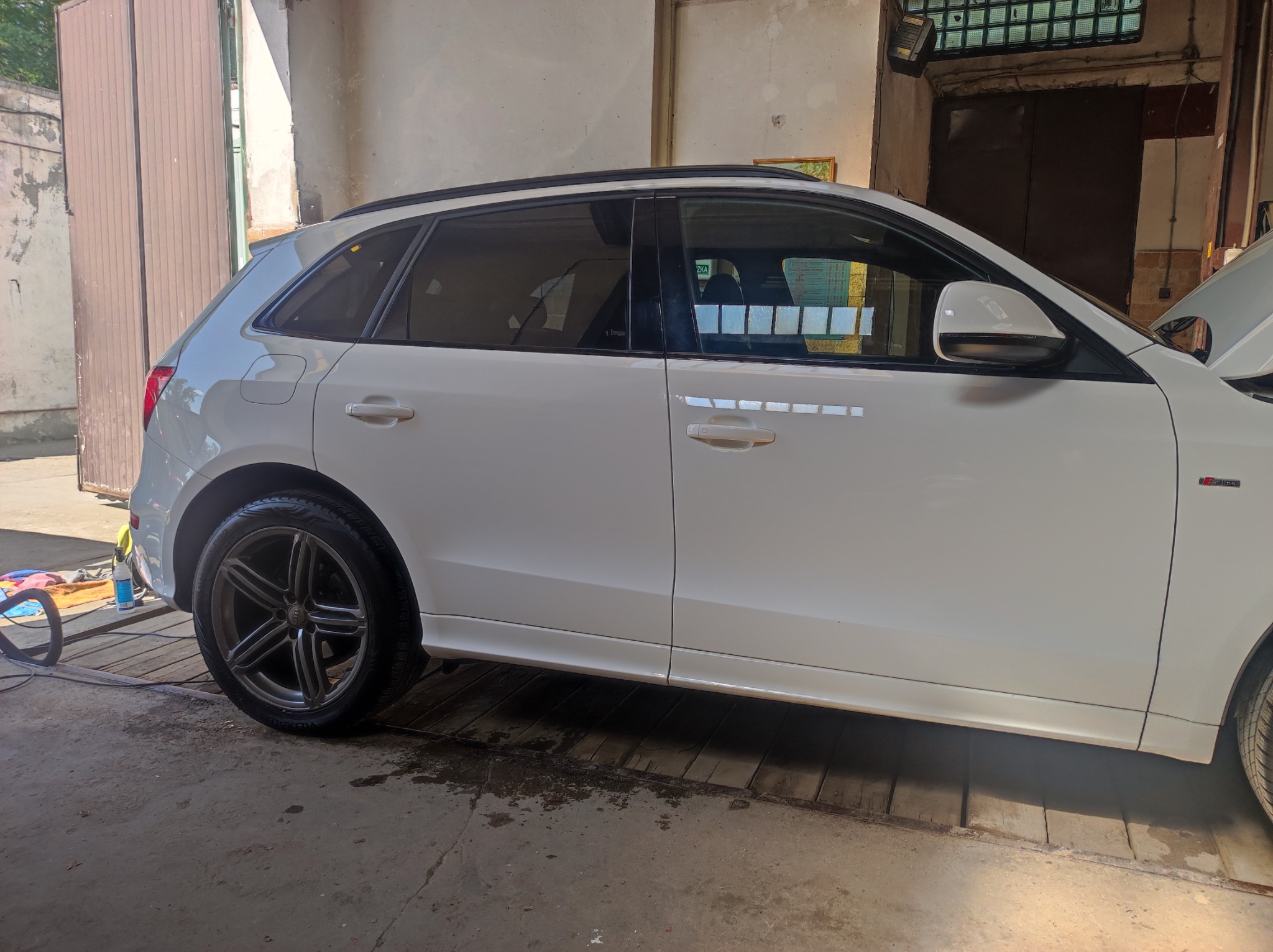 Biały samochód typu SUV marki Audi, model Q3, po umyciu, z mokrą oponą i widocznymi śladami wody na podłodze myjni.