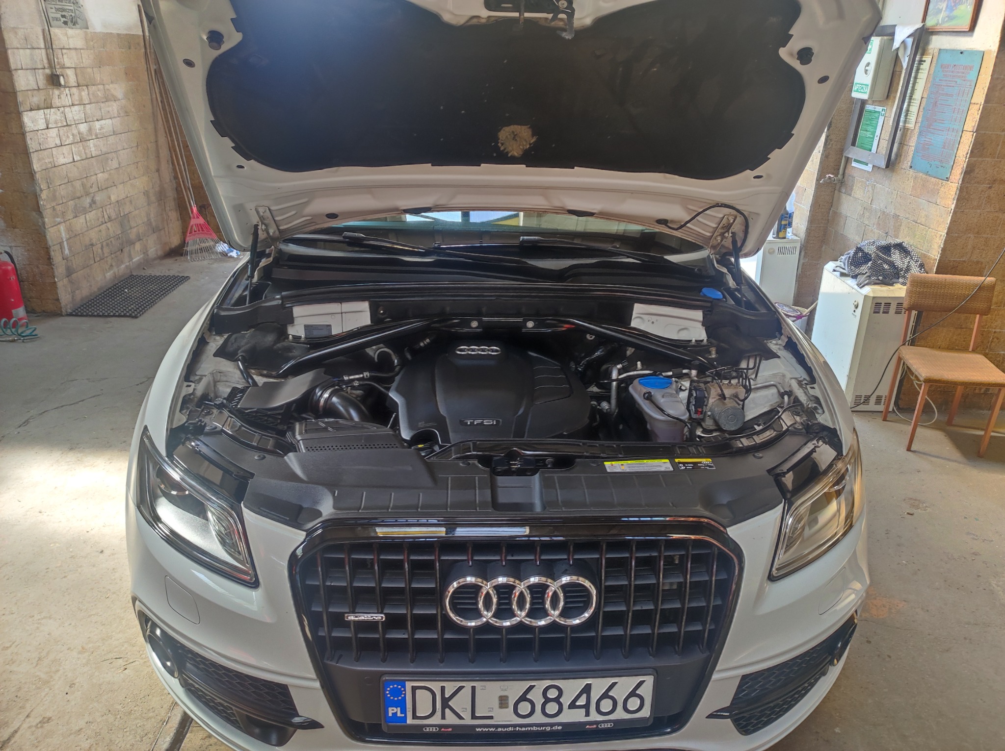 Otwarta maska białego Audi Q5 z widocznym silnikiem TFSI w warsztacie, numer rejestracyjny DKL 68466.