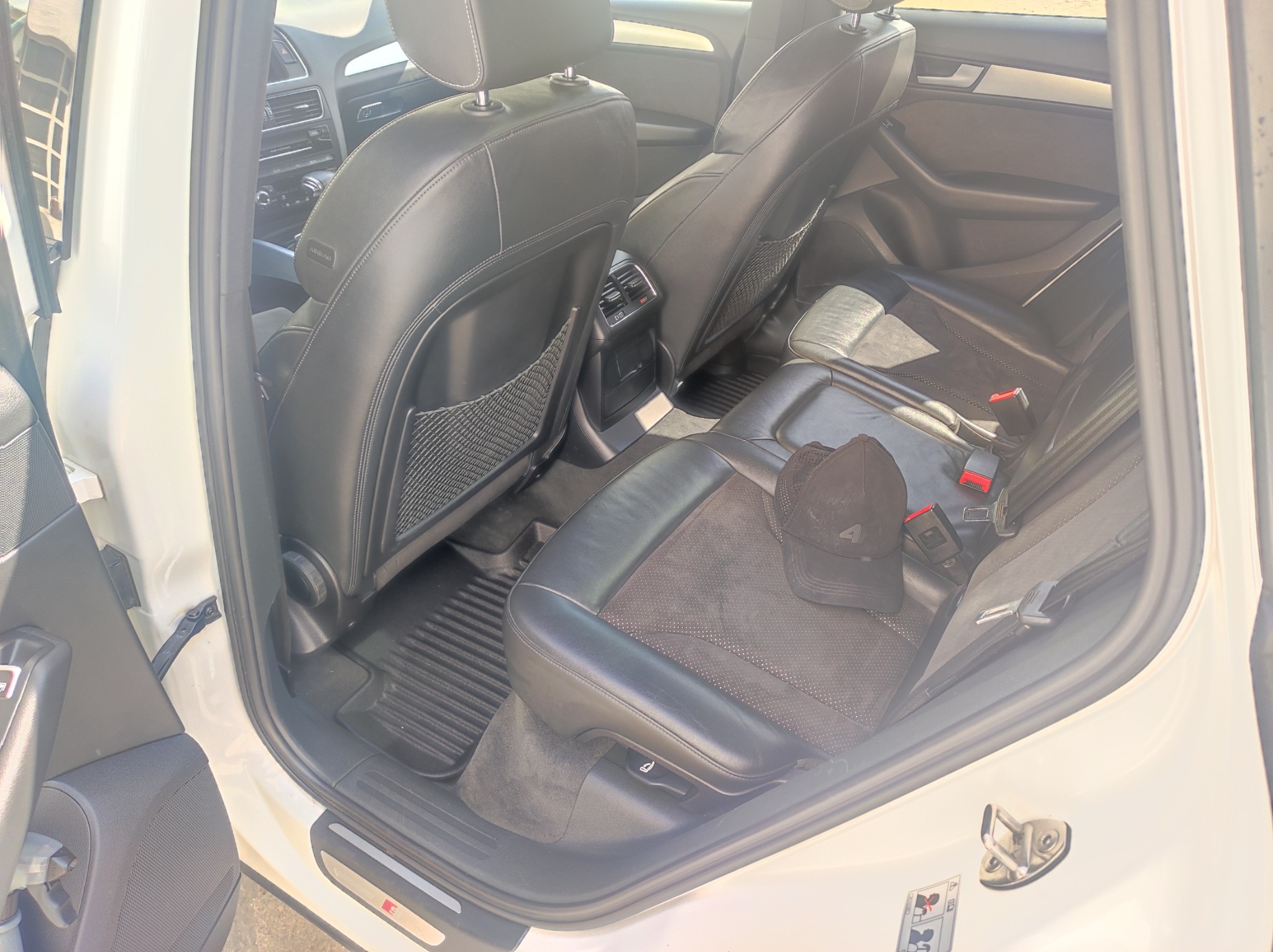 Wnętrze samochodu z czarnymi skórzanymi siedzeniami, widok z otwartych tylnych drzwi, czapka leżąca na siedzeniu.