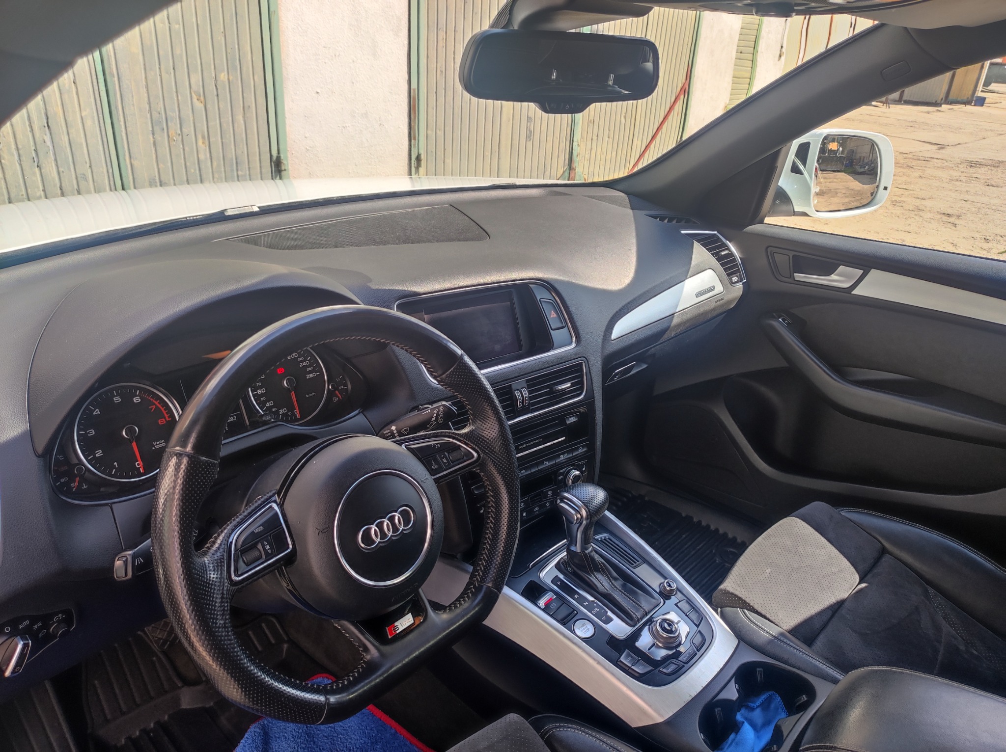 Wnętrze samochodu Audi Q5 z czarną skórzaną tapicerką, widok na kierownicę, deskę rozdzielczą i konsolę środkową, z elementami srebrnego wykończenia i widocznym logo Audi na kierownicy.