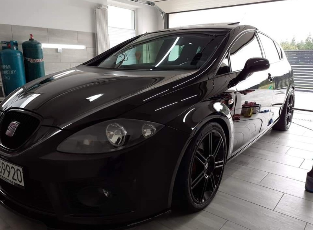 Błyszczący, czarny samochód Seat Leon po detailingu, z widocznymi odbiciami w lakierze, stojący w garażu z butlami gazowymi w tle.