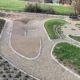 Firma Usługowa 2P inż. Paweł Puto - Widok z góry na ogród w trakcie aranżacji: ścieżki wysypane żwirem z obrzeżami z kostki, przygotowane rabaty ziemne i trawnik, w tle domki letniskowe i trampolina.