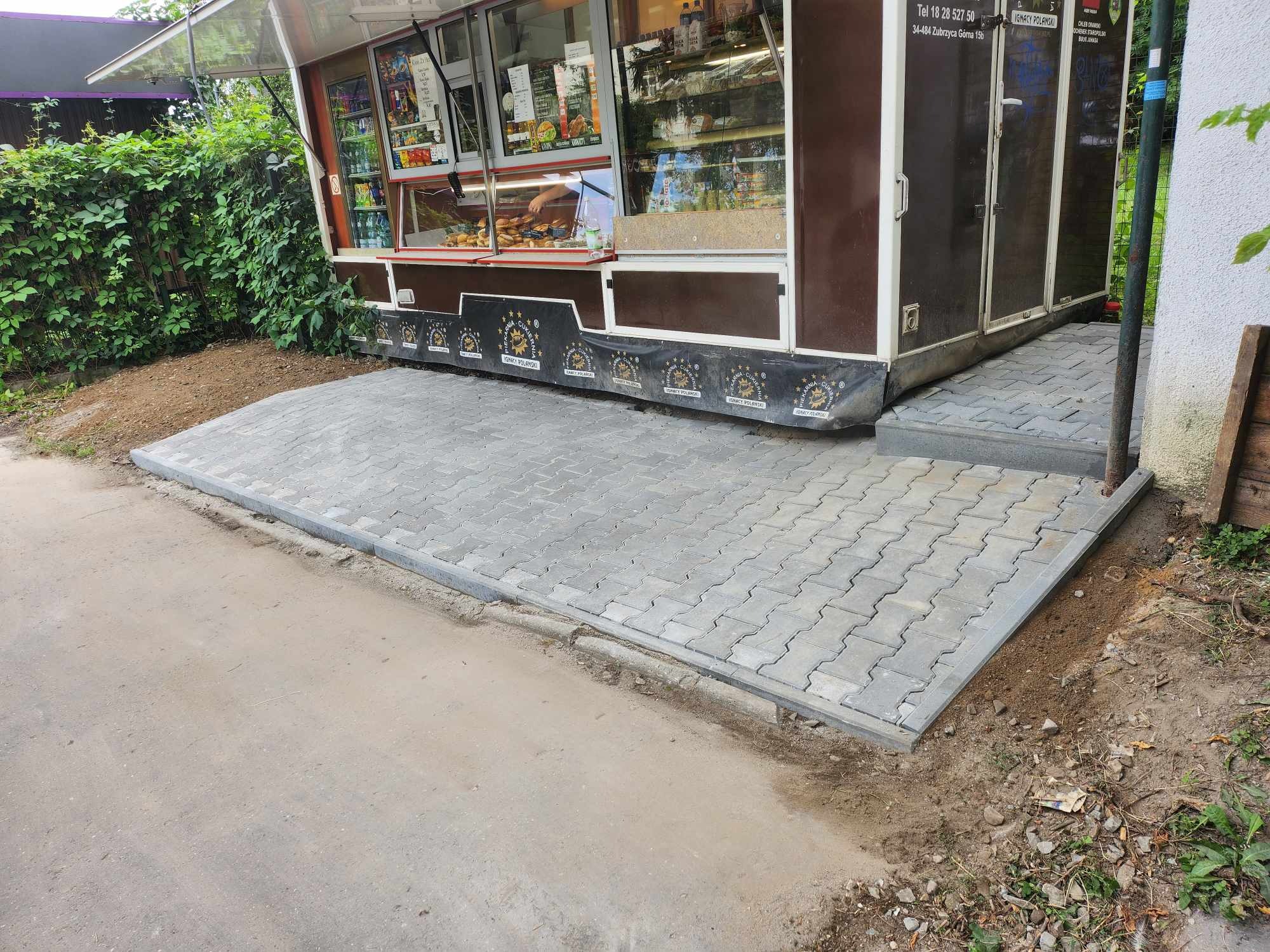 Szara kostka brukowa ułożona jako podjazd do food trucka, z widocznymi obrzeżami i lekkim nachyleniem.