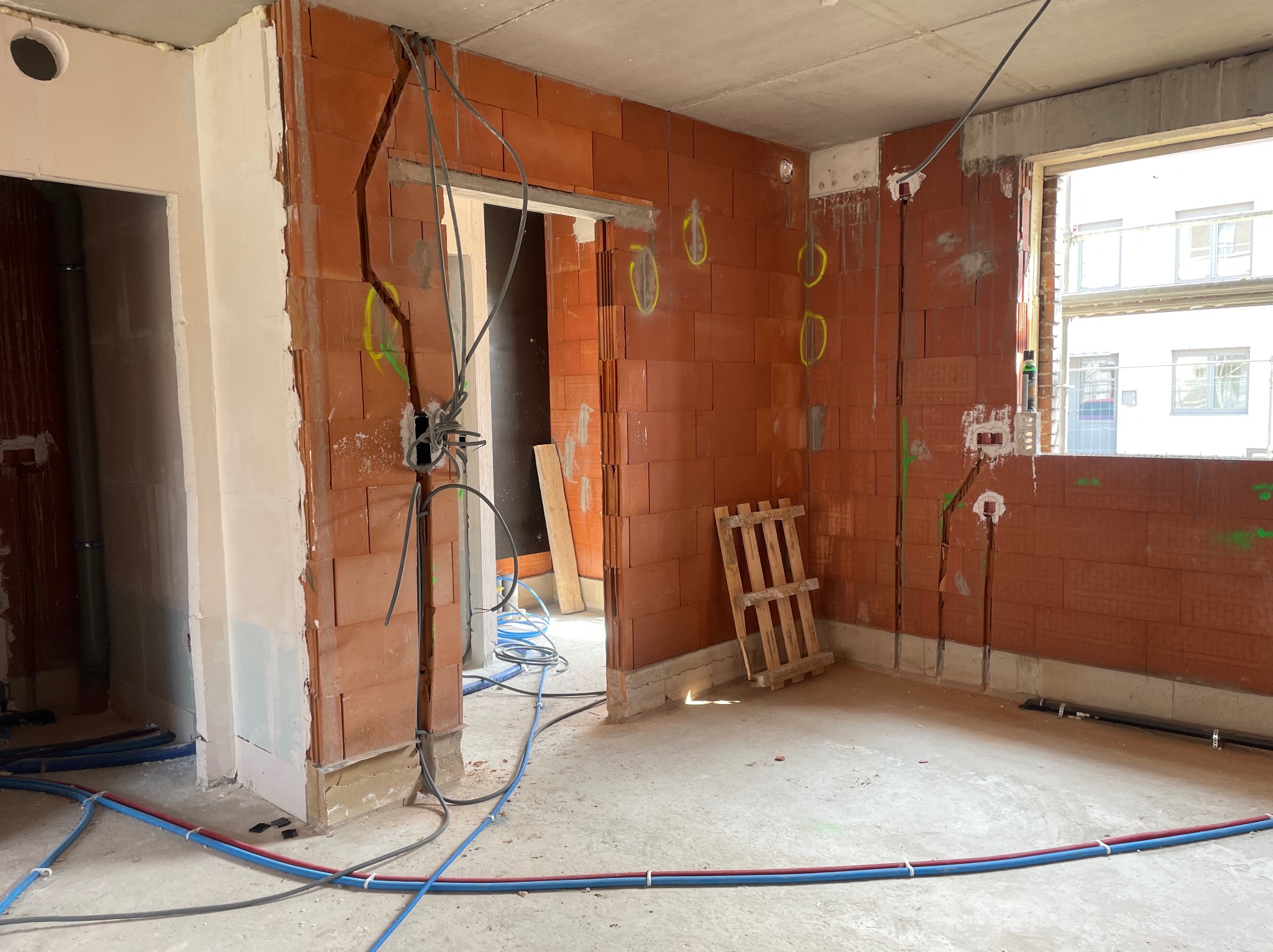 Wnętrze w stanie surowym w Sicienko z instalacją elektryczną w bruzdach ściennych i przewodami ułożonymi na podłodze, widoczne puszki elektryczne i paleta drewniana.