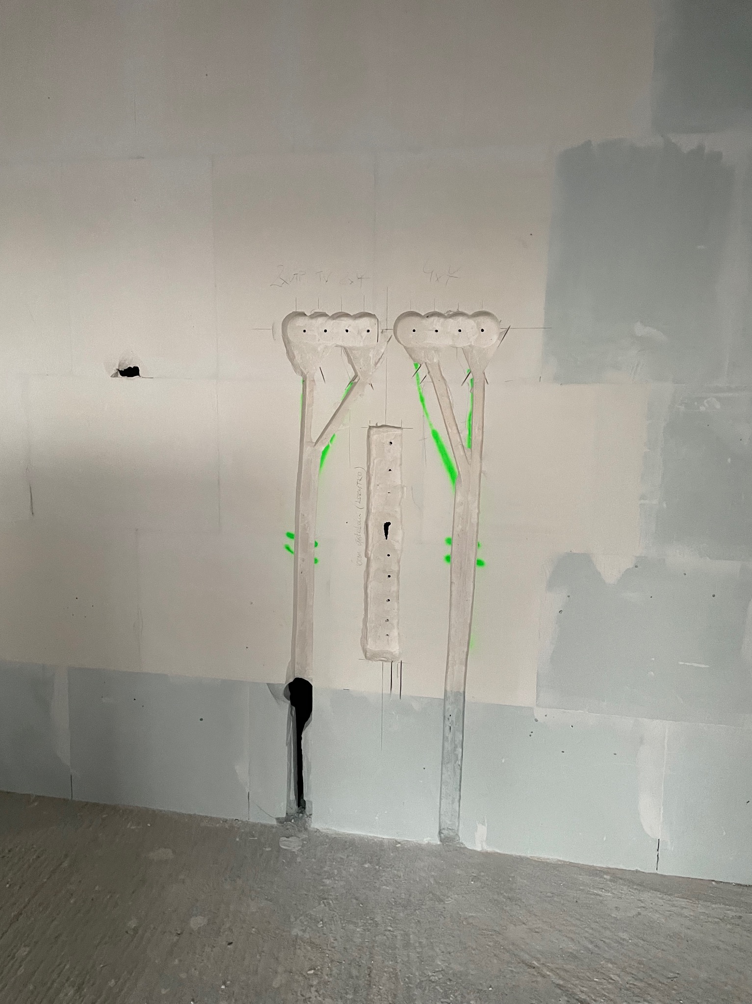 Przygotowanie pod instalację elektryczną w ścianie z wyciętymi otworami i zaznaczeniami, widoczne pionowe bruzdy i otwory na przewody, ściana w trakcie wykończenia.