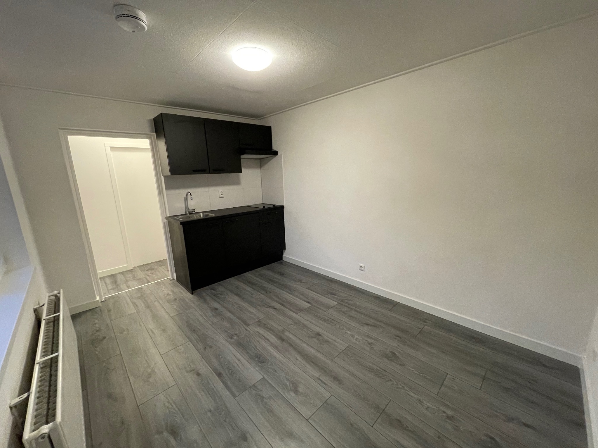 Mała, nowa kuchnia z czarnymi szafkami i szarymi panelami podłogowymi, widok z perspektywy wejścia do pomieszczenia.