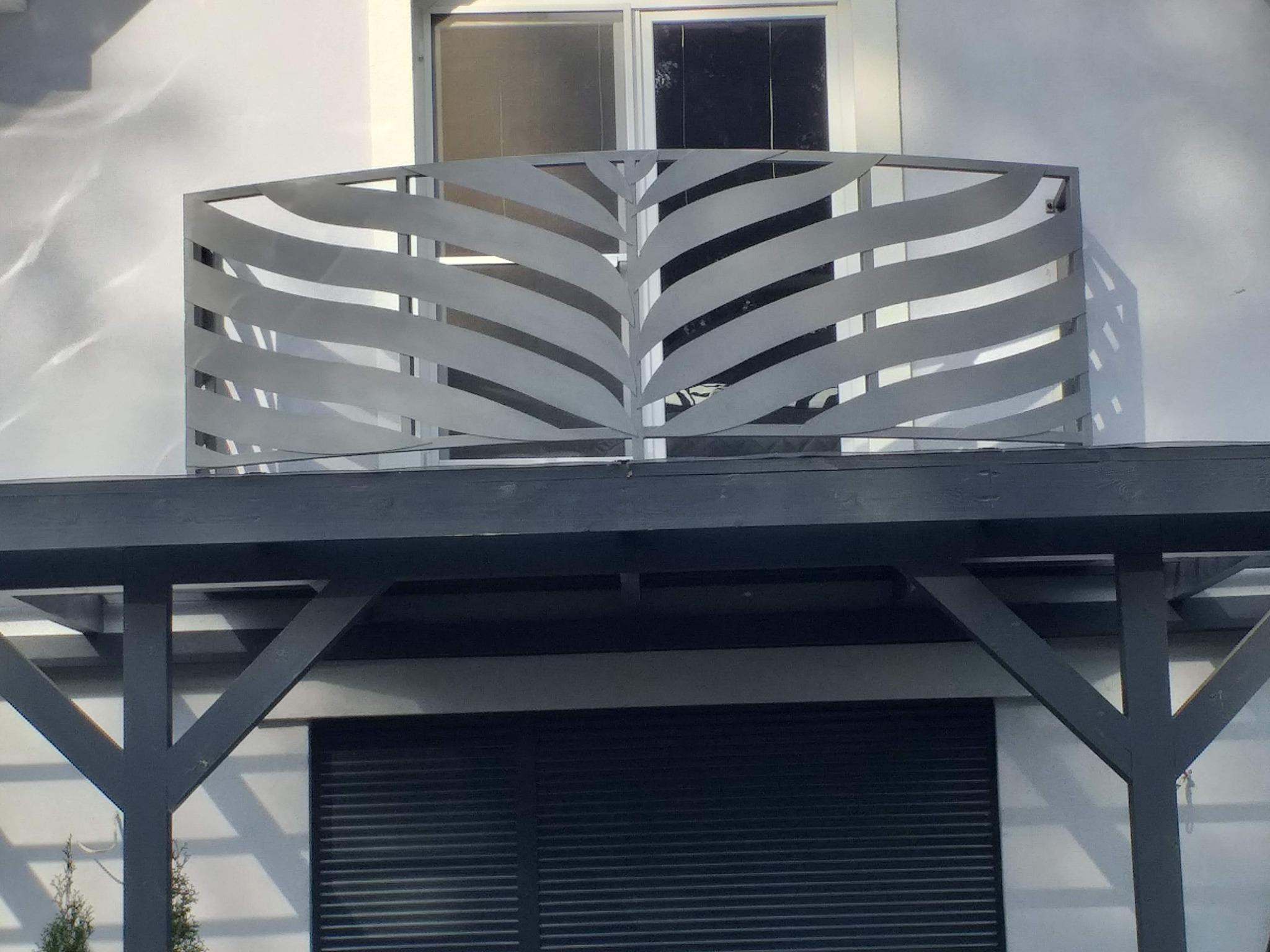 Nowoczesna, metalowa balustrada balkonowa z motywem liściastym, zamontowana na balkonie budynku z białym tynkiem.