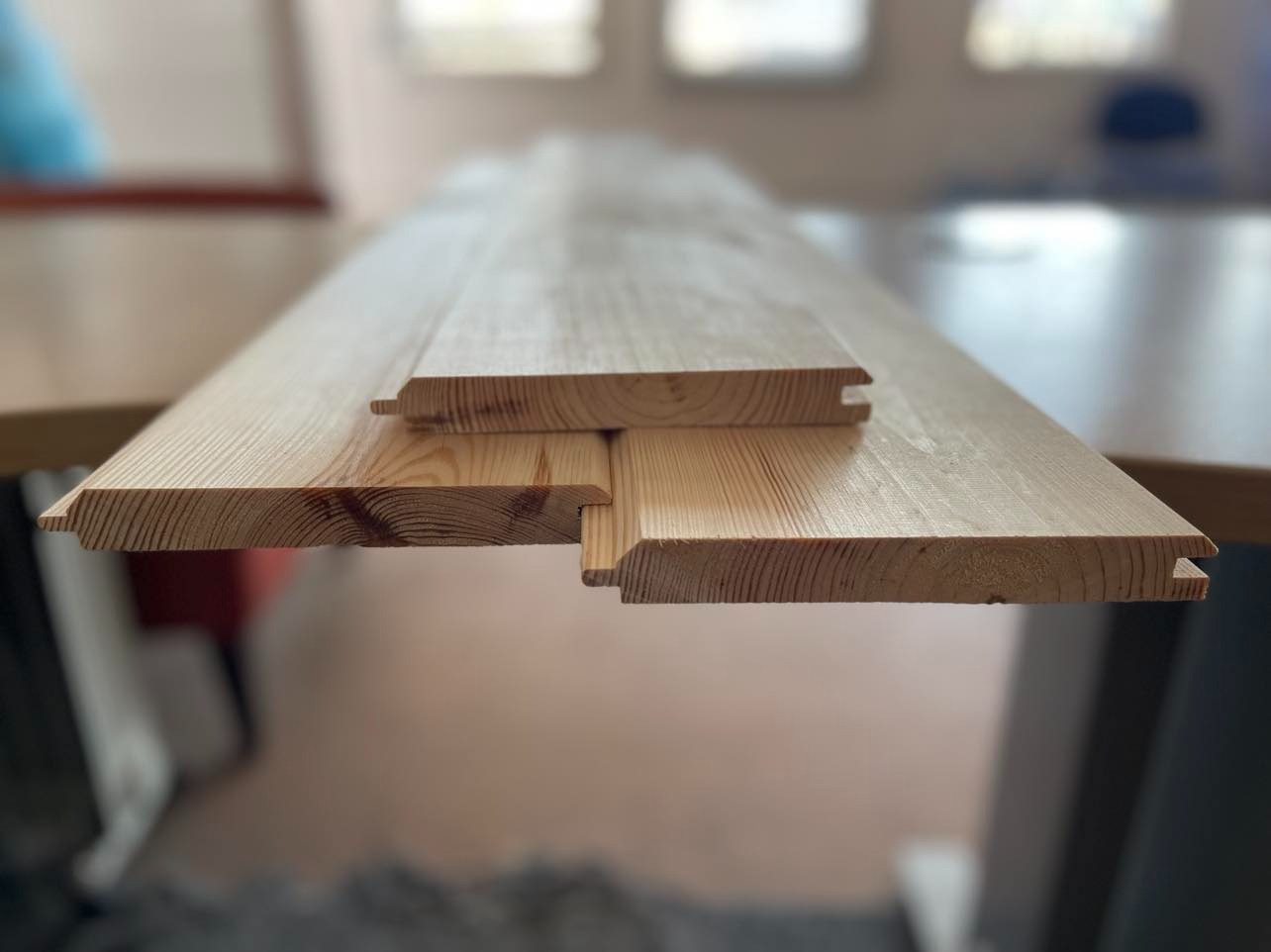 Profilowane deski boazeryjne z jasnego drewna, widoczne połączenia pióro-wpust, ułożone na stole w jasnym, rozproszonym świetle.