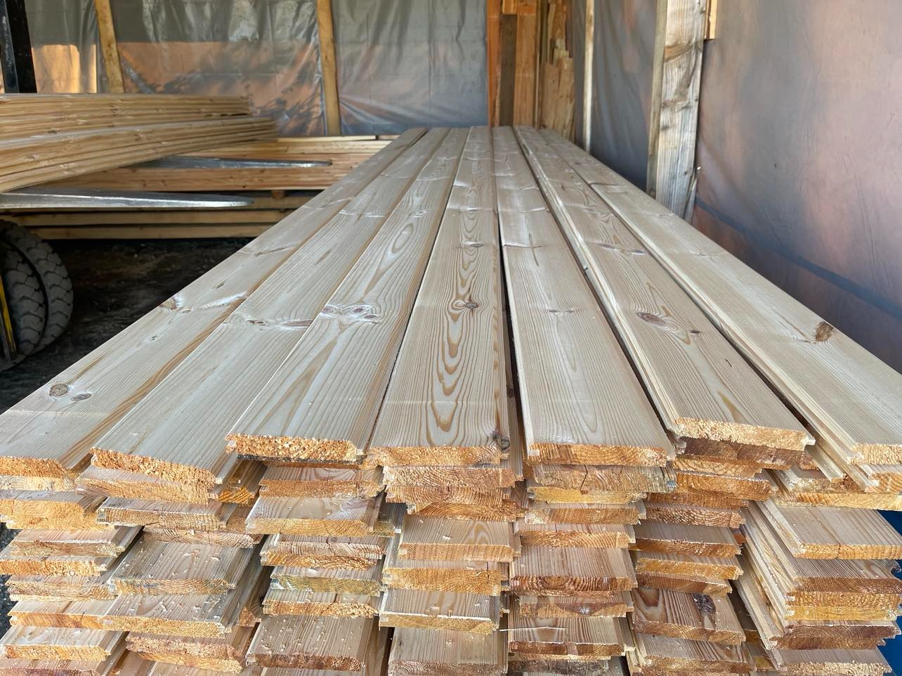 Stos świeżo obrobionych desek sosnowych, ułożonych warstwami, z widocznymi słojami drewna i drobnymi wiórami na krawędziach, prawdopodobnie przygotowanych do dalszej obróbki lub transportu.