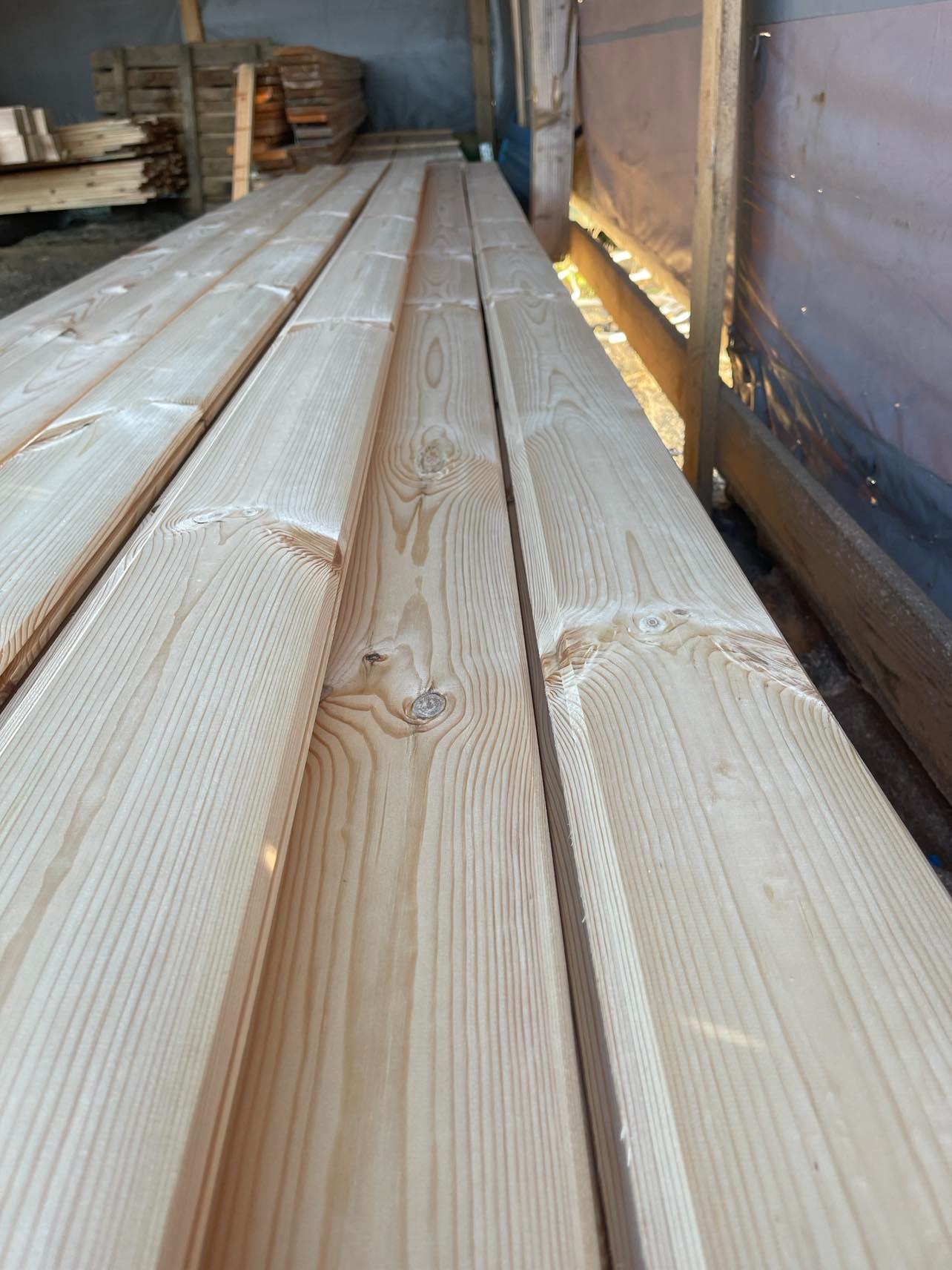 Stos jasnych, heblowanych desek z widocznym usłojeniem i małymi sękami, ułożonych równolegle w magazynie.
