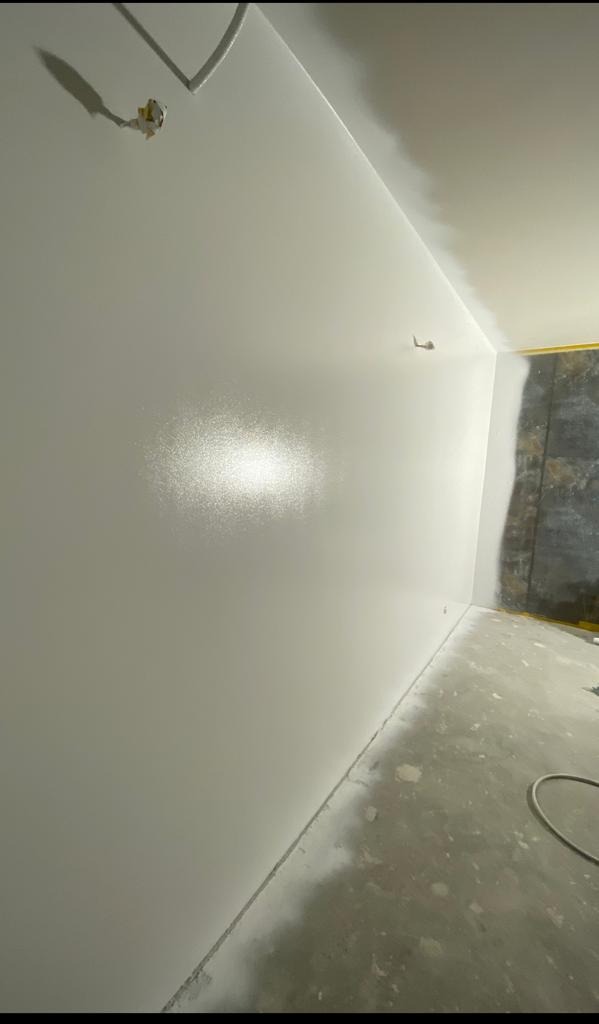 Świeżo pomalowane na biało wnętrze z widocznymi śladami po taśmie malarskiej na podłodze i zaklejonym gniazdkiem elektrycznym, ukazujące etap prac wykończeniowych.