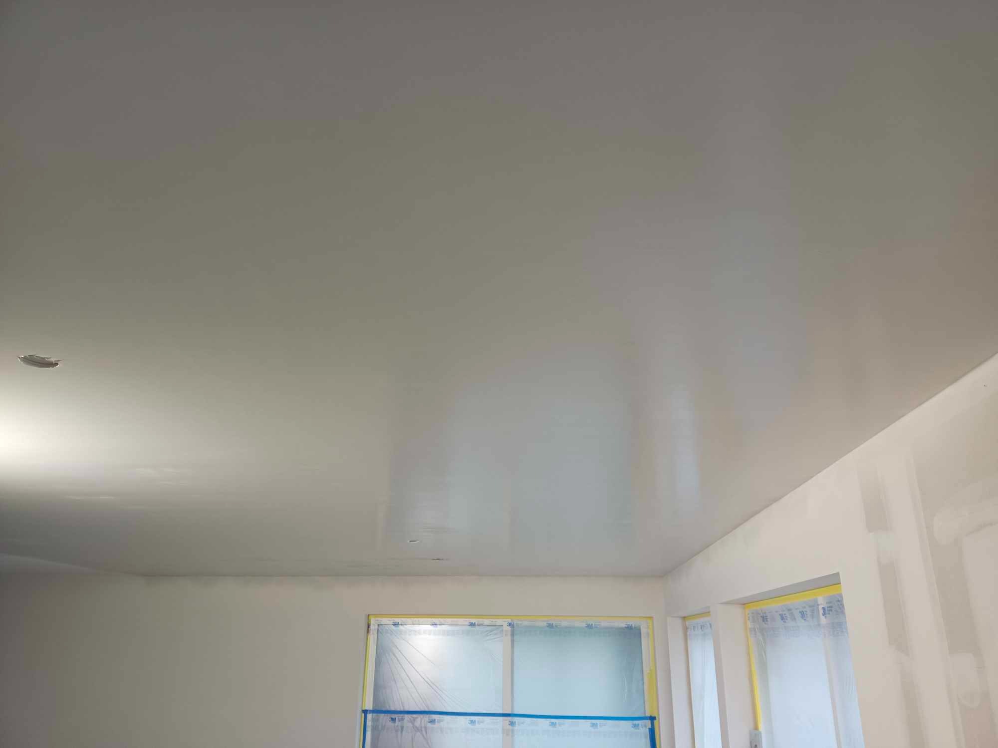 Świeżo położona, jasnoszara gładź na suficie i ścianach, okno zabezpieczone folią malarską, widoczne delikatne smugi po nakładaniu gładzi.