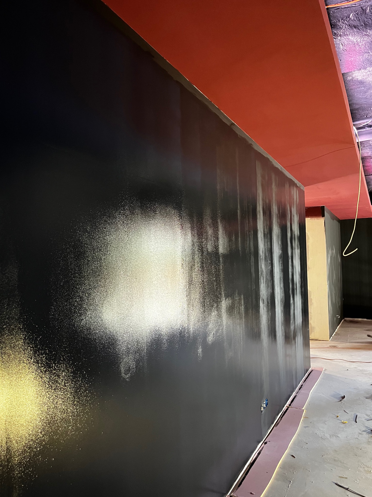 Częściowo pomalowana na czarno ściana wewnętrzna z widocznymi smugami farby i czerwonym sufitem, w trakcie prac wykończeniowych.