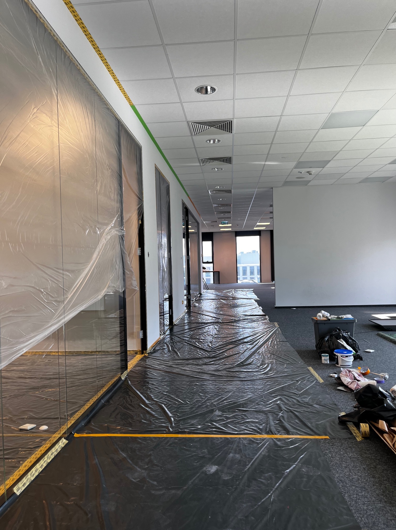 Przygotowanie biura do odświeżenia: folia ochronna na podłodze i taśma malarska zabezpieczająca szklane ściany działowe przed zabrudzeniem.