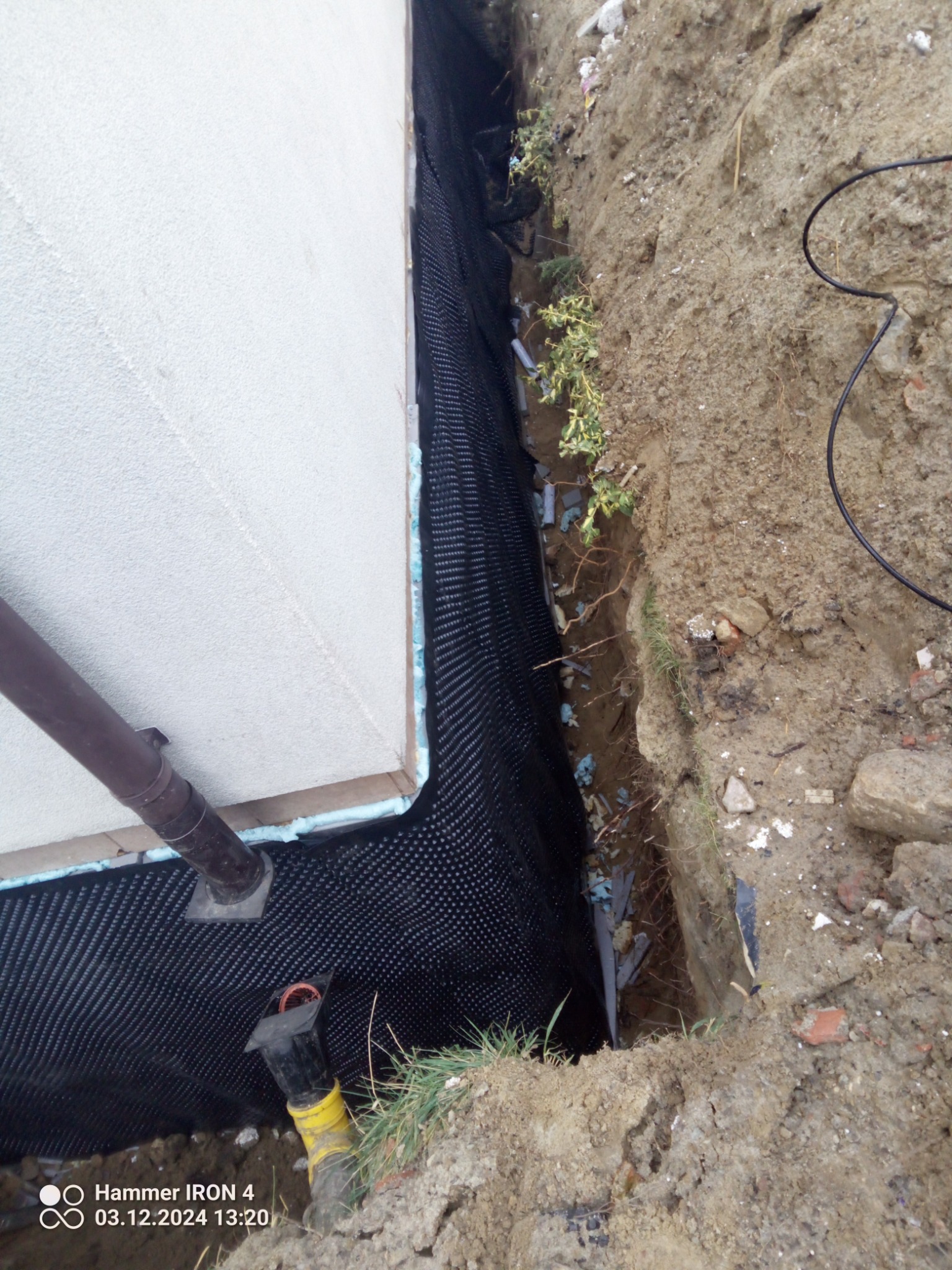 Ocieplenie fundamentów budynku z widoczną folią kubełkową i izolacją termiczną, zabezpieczone przed wilgocią gruntu. Widoczny rów wykopany w ziemi.