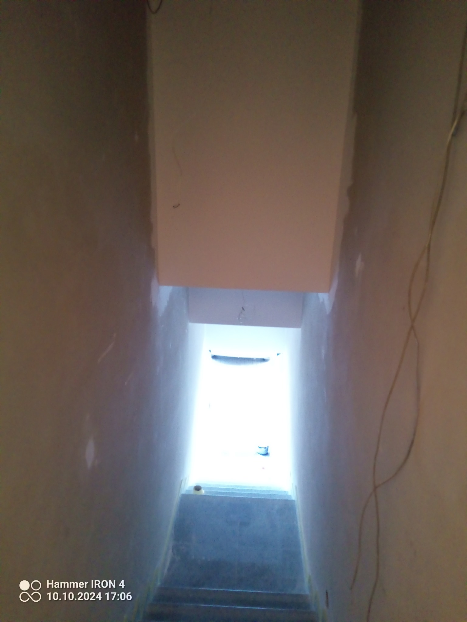 Wnętrze klatki schodowej w trakcie remontu. Widoczne świeżo pomalowane ściany, schody i fragment sufitu z widocznymi śladami szpachlowania. W tle jasne światło wpadające z zewnątrz.