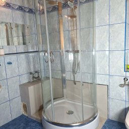 Pielęgnacja użytków zielonych - Zamontowana narożna kabina prysznicowa z chromowanymi elementami i przezroczystymi drzwiami, w łazience z jasnoniebieskimi płytkami ściennymi z ozdobnym paskiem i ciemnoniebieskimi płytkami...