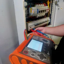 Elektryk mierzy parametry w rozdzielnicy elektrycznej za pomocą miernika Sonel MPI 530, widoczne przewody i zabezpieczenia.