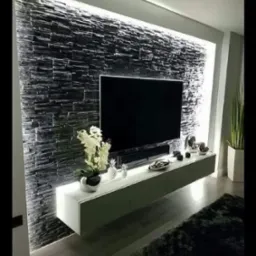 Nowoczesny salon z czarną ścianą z kamienia dekoracyjnego podświetloną LED, wisząca biała szafka RTV z dekoracjami i roślinami, czarny telewizor.