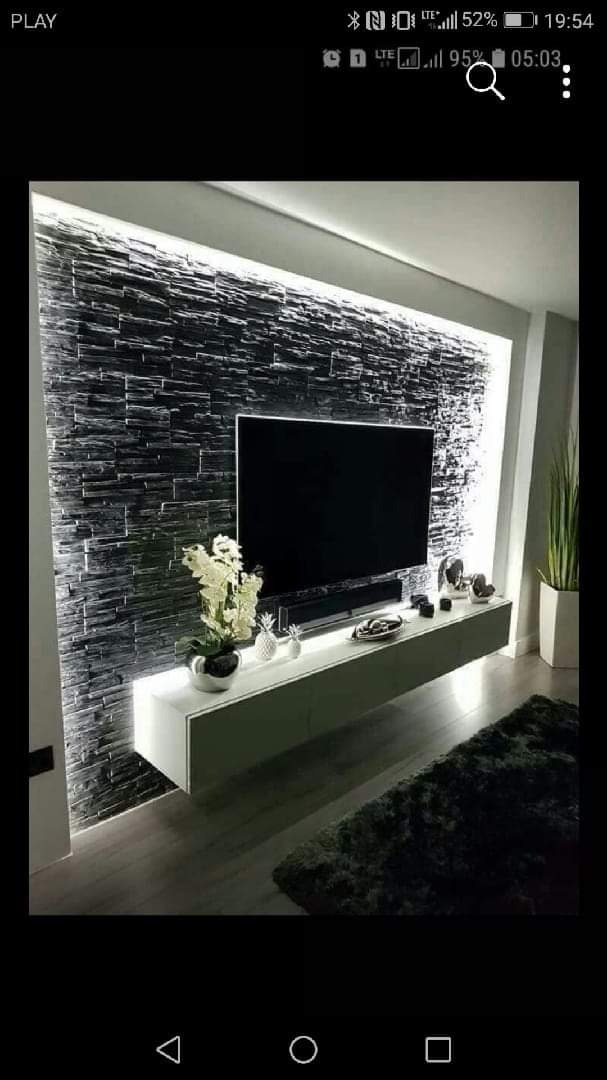 Nowoczesny salon z czarną ścianą z kamienia dekoracyjnego podświetloną LED, wisząca biała szafka RTV z dekoracjami i roślinami, czarny telewizor.