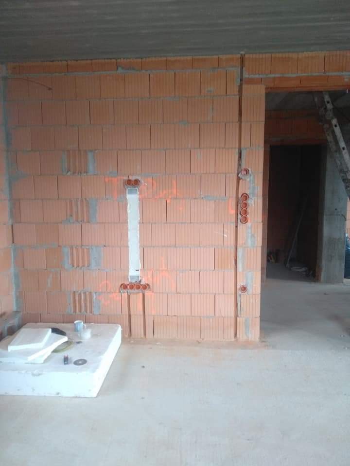 Wykute bruzdy w ceglanej ścianie pod instalację elektryczną, widoczne puszki instalacyjne i oznaczenia tras kabli czerwoną farbą, surowy stan wykończenia wnętrza.