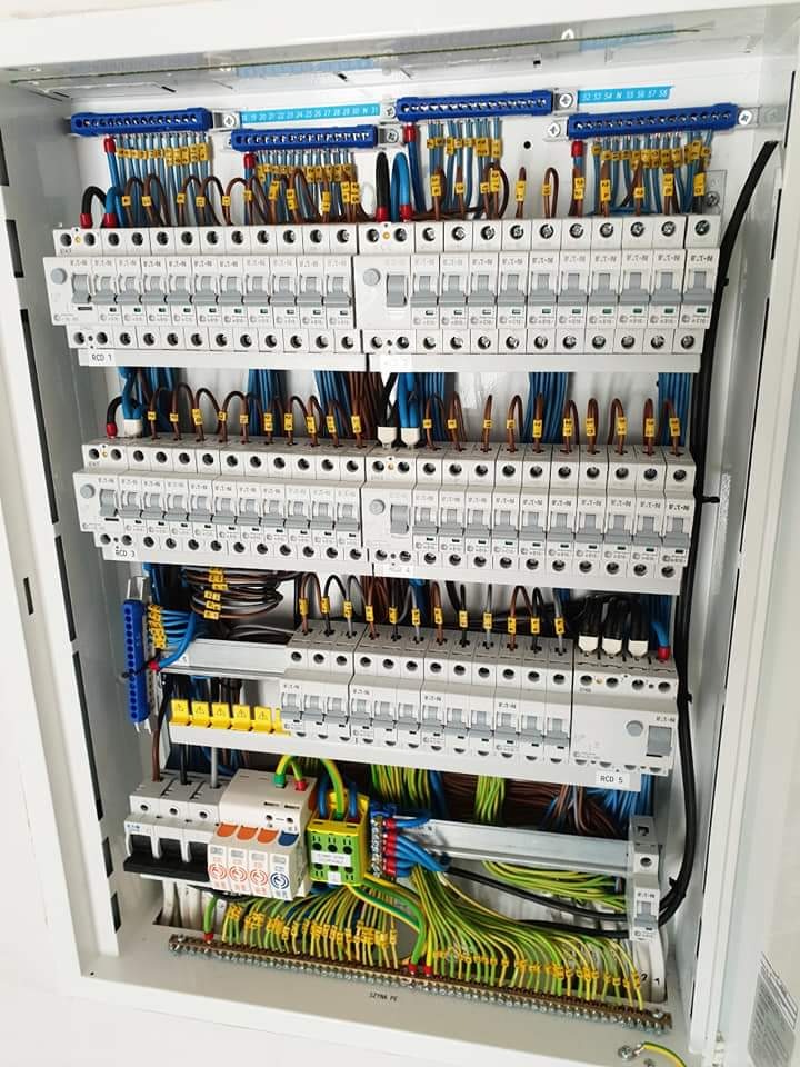 Rozdzielnica elektryczna z zainstalowanymi bezpiecznikami, okablowaniem oznaczonym tulejkami i listwami zaciskowymi, zamontowana w białej obudowie.