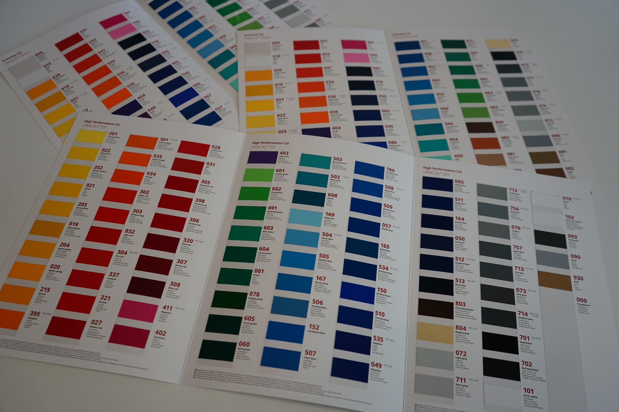 Wzorniki kolorów farb i folii samoprzylepnych marki Oracal, prezentujące szeroką gamę odcieni z numeracją i nazwami, rozłożone na białym tle.